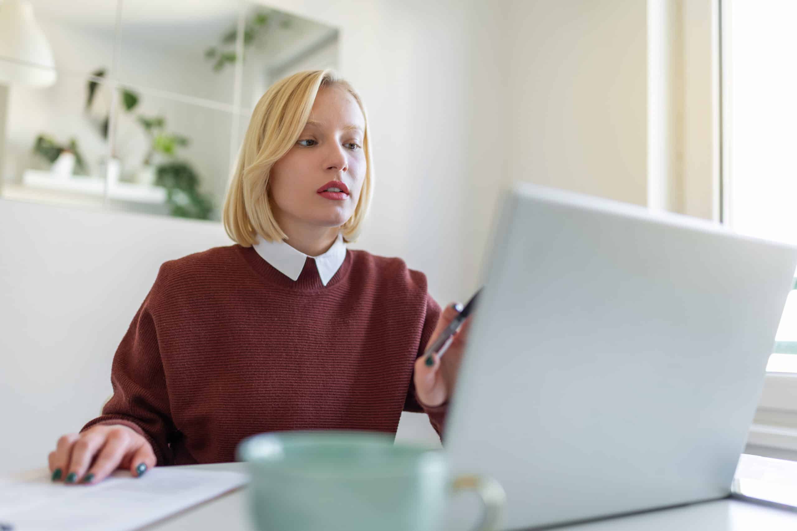 A young woman works remotely on a laptop in her apartment.