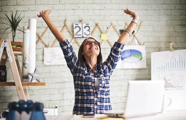 Woman at computer with hands raised happily