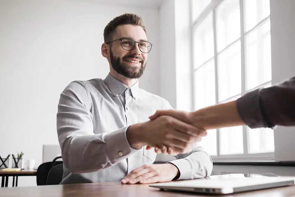 White male shakes coworkers hand while sitting at desk