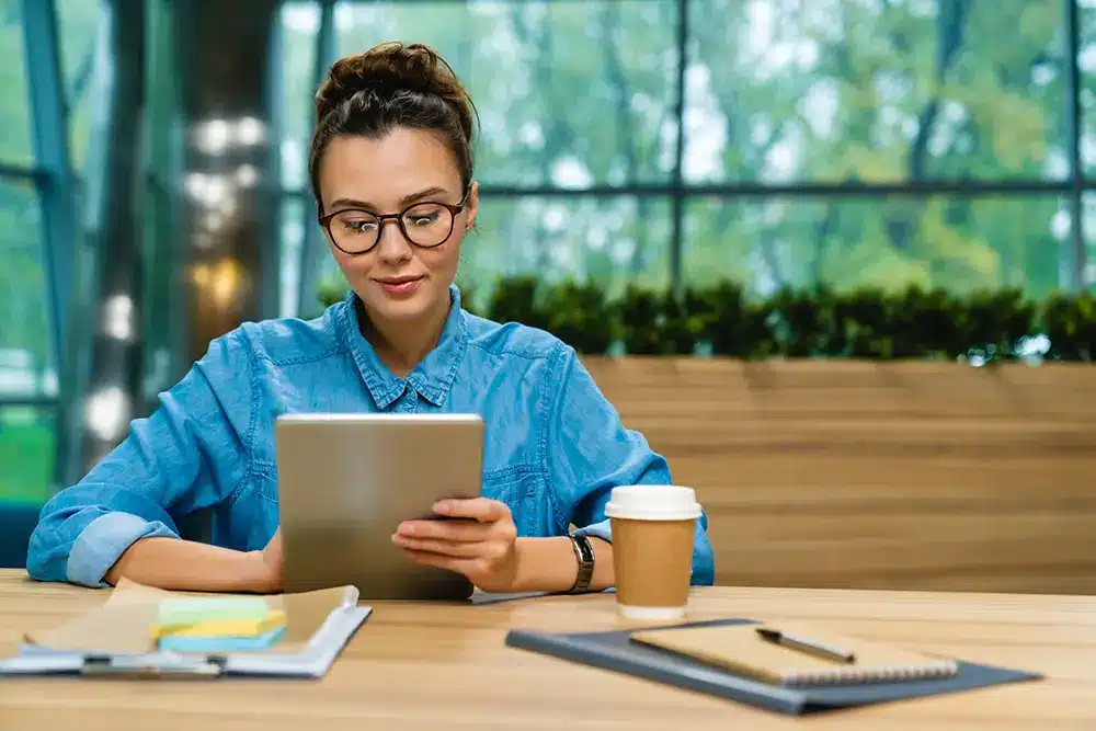 Woman sits at table using a digital tablet