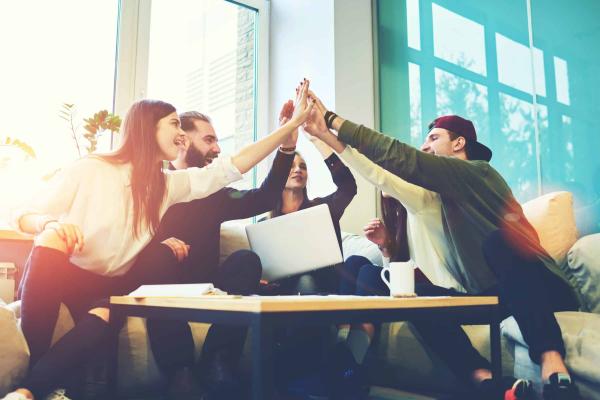 Coworkers high fiving at a table large window behind