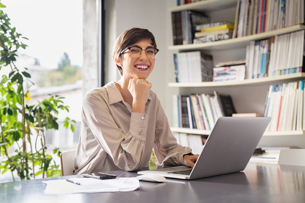 young woman with short hair smiling as she looks up from her computer