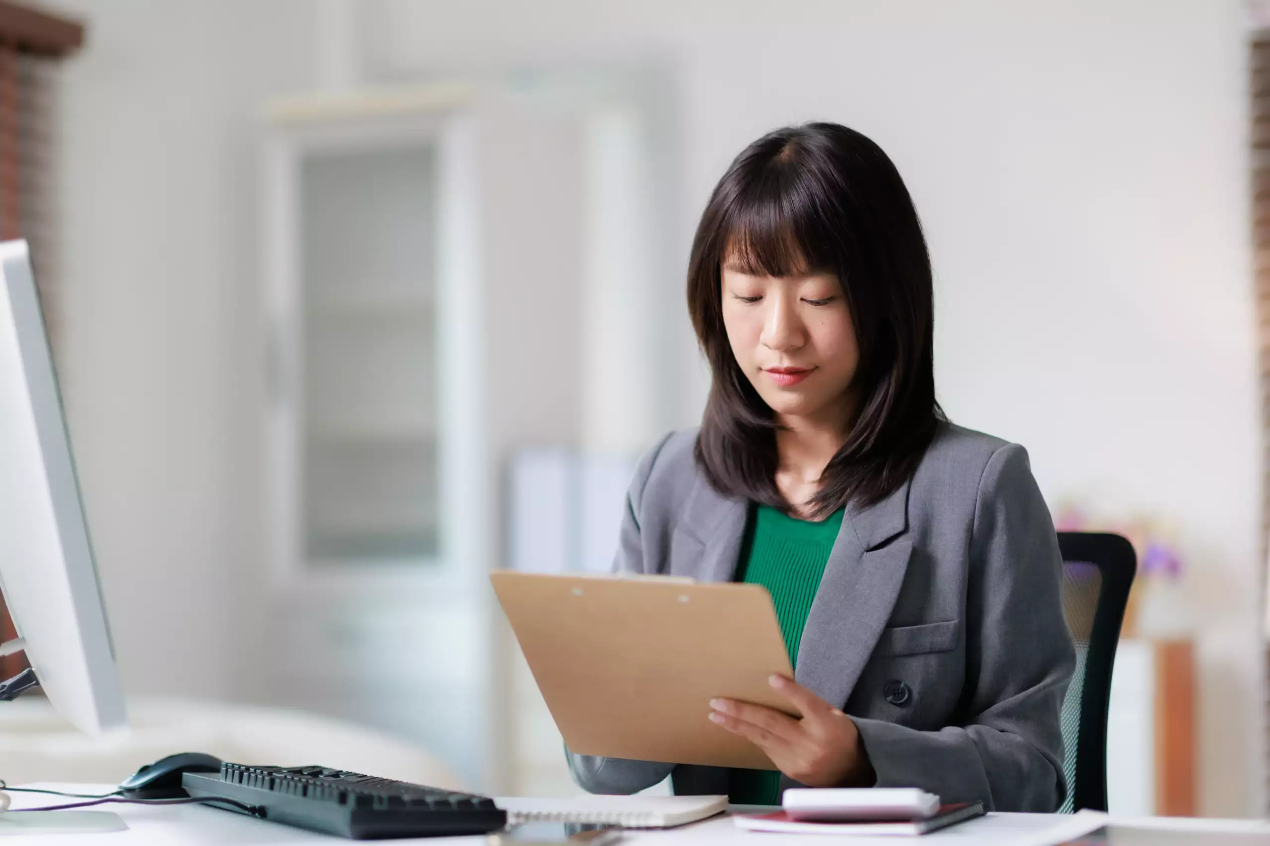 business-woman-reviewing-reports-and-notes Business professional reviewing reports and notes at an office workstation